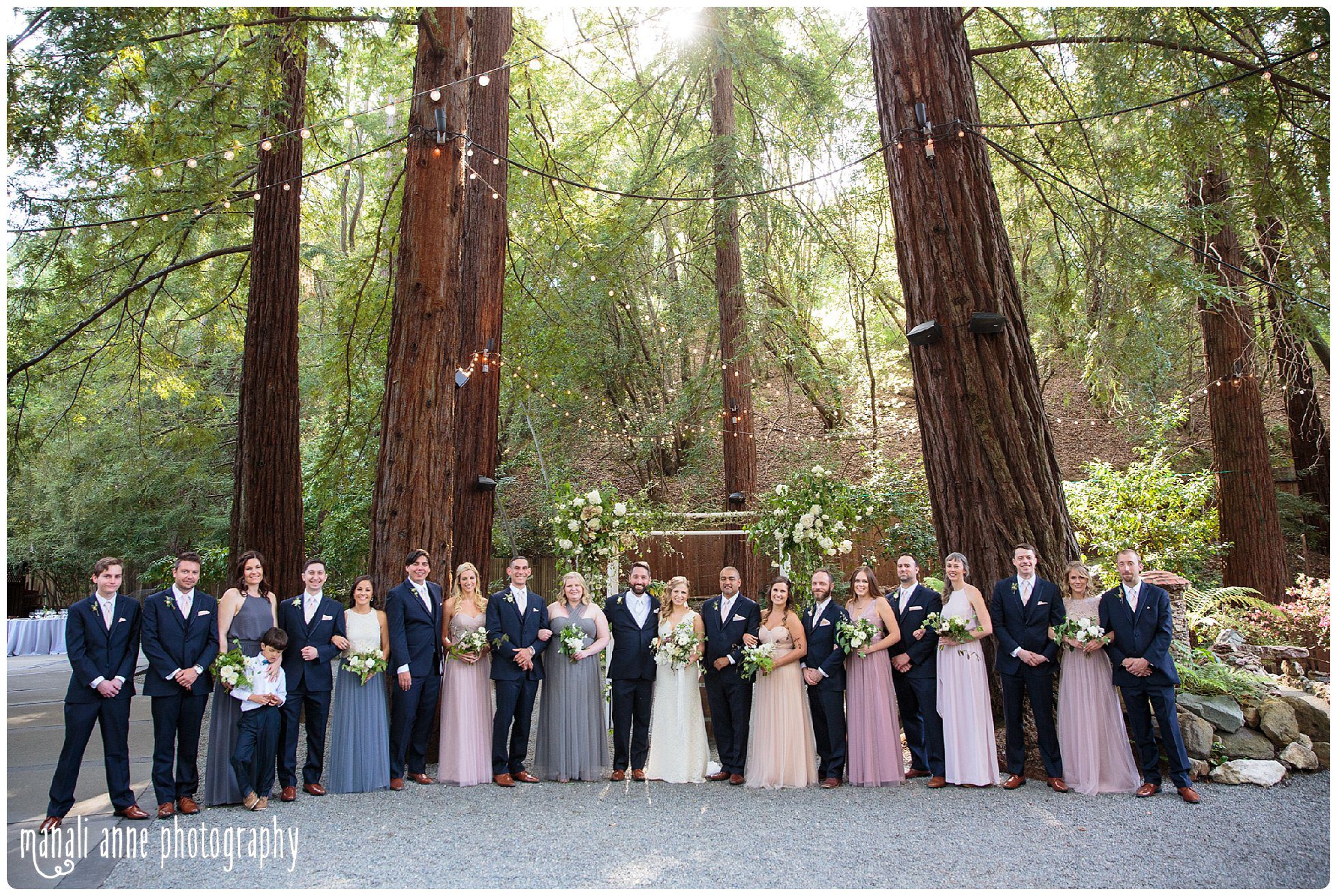 Full wedding party stands together inside the Deer Park Villa redwood grove